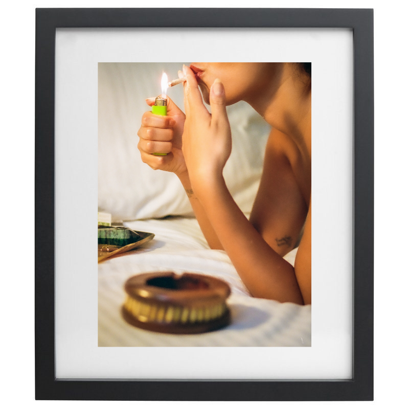 Photograph of a woman smoking on a bed in a black frame